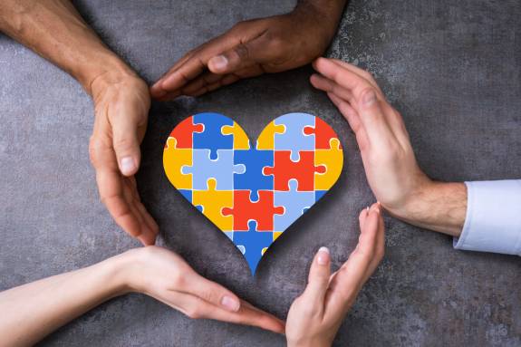 Mehrere Hände formen einen Kreis um ein Herz aus Puzzleteilen
