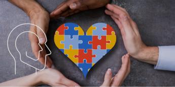 Mehrere Hände formen einen Kreis um ein Herz mit Puzzleteilen
