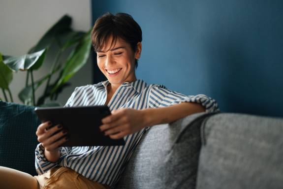 Porträt einer glücklichen Frau, die sich auf dem Sofa ausruht und ein digitales Tablet benutzt